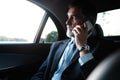 Mature smiling man talking over phone while sitting in taxi. Businessman talking over cellphone while commuting. Royalty Free Stock Photo