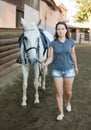 Mature smiling woman farmer standing with white horse at stable Royalty Free Stock Photo