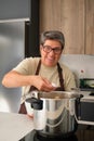 Mature Spanish woman adding salt to the stew in a pressure cooker.