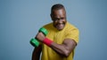 Mature strong athletic man coach pumping biceps with dumbbell in studio on gray background doing exercise pumps up