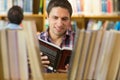 Mature student reading book by shelf in the library Royalty Free Stock Photo