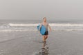 Mature surfboarder holding blue surfboard in hand, carrying sporty equipment coming out of waving sea after surfing. Royalty Free Stock Photo