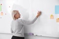 Mature teacher writing on whiteboard in classroom Royalty Free Stock Photo