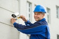 Mature Technician Installing Camera On Wall With Screwdriver