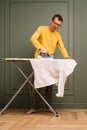 Mature man in glasses ironing snow-white shirt on pressboard using flatiron. Soigne tall human working around house. Royalty Free Stock Photo
