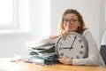 Mature tired woman with clock at table in office. Time management concept