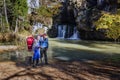 Mature tourists with backpacks stand at the Atysh waterfall flowing from the Big Grotto of the Ural Mountains