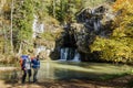 Mature tourists with backpacks stand at the Atysh waterfall flowing from the Big Grotto of the Ural Mountains