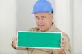 mature tradesman holding blank sign with green background