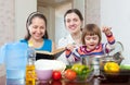 Mature woman and adult daughter with baby girl cook vegetables