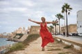 Mature woman, beautiful, blonde, with a red dress, walking with open arms, grateful, full of happiness, while the wind blows her