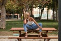 Mature woman, beautiful, blonde, with white top and jeans, in a funny, flirtatious and sensual attitude, sitting on a wooden bench