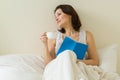 Mature woman in bed reading book and drinking morning coffee Royalty Free Stock Photo
