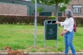 Mature woman in casual clothing depositing her dog`s waste in a public rubbish bin on the street