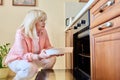 Mature woman with dish of baking apples cooking in oven, at home in kitchen