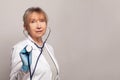 Mature woman doctor in medical uniform standing and holding stethoscope on grey studio background. Royalty Free Stock Photo