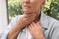 Mature woman doing thyroid self examination near window, closeup