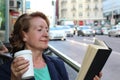 Mature woman drinking coffee and reading book sitting indoor in urban cafe. Cafe city lifestyle with traffic lights Royalty Free Stock Photo