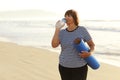 mature woman drinking water from bottle after fitness exercises or yoga on beach by sea. fitness and healthy lifestyle Royalty Free Stock Photo