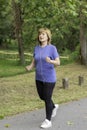 Mature woman with dyed hair jogging along a cement path among the nature of a park in Spain Royalty Free Stock Photo