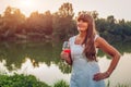 Mature woman enjoying glass of wine by river in autumn park. Senior woman admires landscape Royalty Free Stock Photo