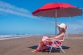 Mature woman enjoying the view while relaxing sitting on a beach chair under an umbrella. Royalty Free Stock Photo