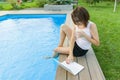 Mature woman freelancer uses a laptop sitting by the pool. Middle-aged woman blogger on a background of nature, yard, home pool is Royalty Free Stock Photo