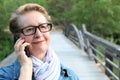 Mature woman with glasses waiting your call. Dressed in a denim jacket, a senior Caucasian lady is standing by river bridge Royalty Free Stock Photo