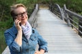 Mature woman with glasses waiting your call. Dressing in a denim jacket, a senior Caucasian lady is standing by river bridge Royalty Free Stock Photo