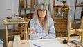 Mature woman with grey hair posing in a carpentry workshop, surrounded by tools and woodwork projects Royalty Free Stock Photo