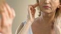 Mature woman heavily sighing looking at her wrinkled and sagging skin in mirror