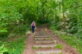 Mature woman with her dog with her back to the camera climbing a hill next to a stone staircase in the middle of the forest