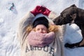 Mature woman in her fifties with red curly hair lies in the snow with gloves, hat and scarf and a dog licks her face with its Royalty Free Stock Photo