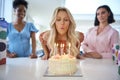 Mature Woman At Home Celebrating Birthday With Friends And Blowing Out Candles On Cake Royalty Free Stock Photo