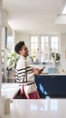 Mature Woman At Home In Kitchen Drinking Coffee And Checking Social Media On Mobile Phone Royalty Free Stock Photo