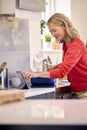 Mature Woman In Kitchen At Home Cooking Meal Following Recipe On Digital Tablet