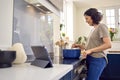 Mature Woman In Kitchen At Home Cooking Meal Following Recipe On Digital Tablet