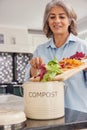 Mature Woman In Kitchen Making Compost Scraping Vegetable Leftovers Into Bin