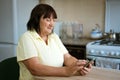 Mature woman in the kitchen at the table with the phone Royalty Free Stock Photo