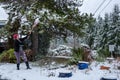 Mature woman knocking wet heavy snow off a pine tree in a garden, snow day