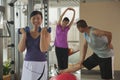 mature woman lifting weights in the foreground, people exercising in the background