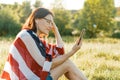 Mature woman listens to music, an audiobook on headphones, relaxes in nature. On the shoulders American flag, background sunset, Royalty Free Stock Photo
