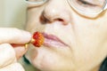 A mature woman looks at a berry of ripe wild strawberry which she holds in her hand.