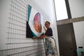 Mature woman painter hanging one of her paintings in her studio. The woman is looking at the camera while smiling. Concept art and Royalty Free Stock Photo