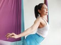 Mature woman pose in hammock performing aerial yoga or flying yoga exercise against white wall background in yoga studio room.