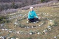 Mature woman practices yoga in the center of a spiral laid out of stones