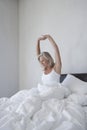 Mature woman in pyjamas sitting in bed under cover stretching in the morning