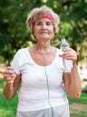 Mature woman quenches her thirst from bottle after jogging in park Royalty Free Stock Photo