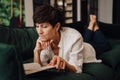 Mature woman reading book while lying on couch Royalty Free Stock Photo