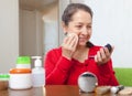 Mature woman in red putting facepowder Royalty Free Stock Photo